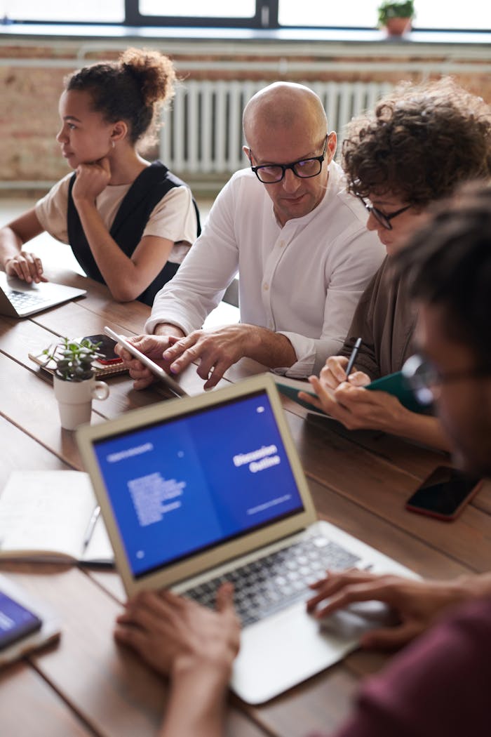 About Diverse team engaged in a collaborative business meeting around a wooden table with laptops.