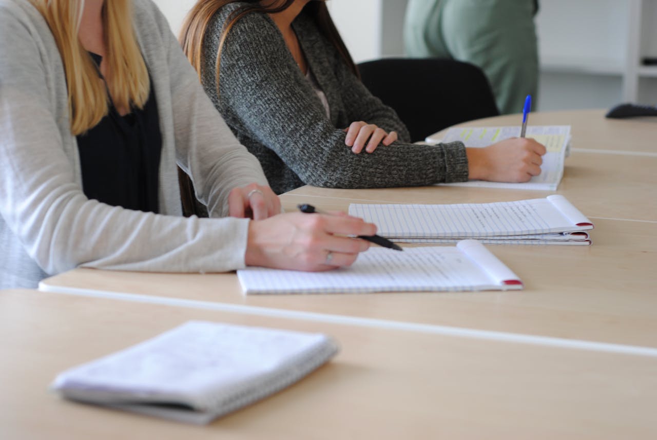 Home Group of students writing notes at a meeting in a well-lit classroom.
